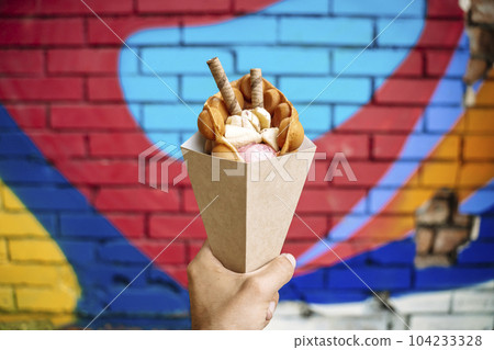 Street food dessert Belgian waffles in hand on a colored wall background. Sweets, street food Street food dessert Belgian waffles in hand on a colored wall background. Sweets, street food 104233328