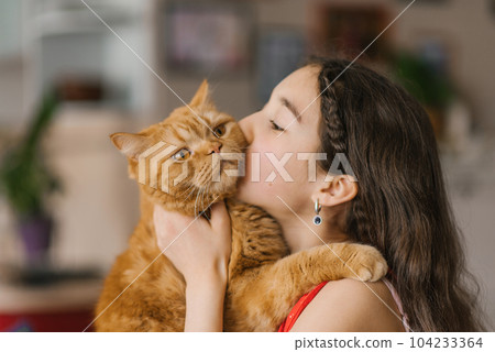 Teenage girl kisses her pet red British cat 104233364