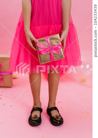 Close up of a girl holding a gift box with a pink silk ribbon, giving a gift for a holiday. Merry Christmas, Happy New Year, Valentine's Day, holiday, festive, Birthday, surprise concept. 104233439