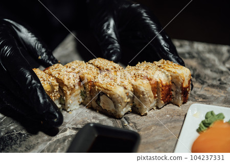 A chef in black gloves stacks a set of rolls to serve to guests. Traditional Japanese food 104237331