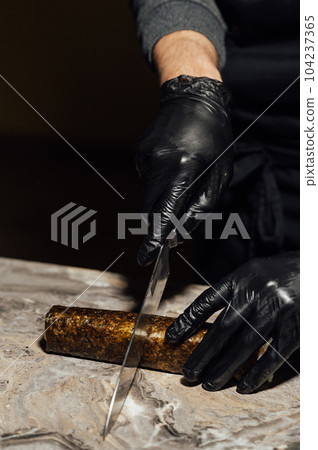 Sushi roll, wrapped in nori, the chef in black gloves cuts with a knife. Sushi is made from raw fish Sushi roll, wrapped in nori, the chef in black gloves cuts with a knife. Sushi is made from raw fish 104237365