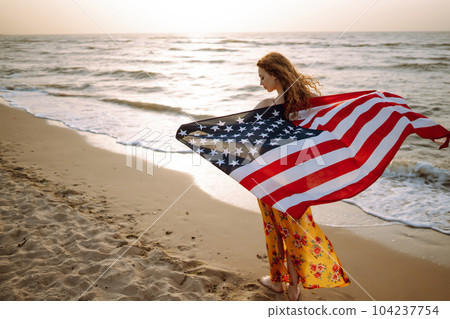 Young woman with american flag on the beach at sunset. 4th of July. Independence Day. 104237754