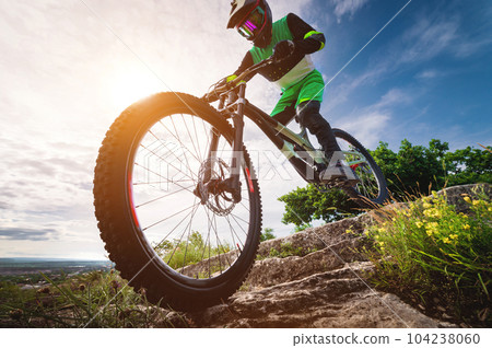 Mountain biker on a stone forest path. A cyclist rides on a rock. Dinehill rider on his mountain bike. Wide angle sun and clouds on background Mountain biker on a stone forest path. A cyclist rides on a rock. Dinehill rider on his mountain bike. Wide angle sun and clouds on background 104238060