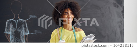 Smiling African-American teacher stands at table against blackbo Smiling African-American teacher stands at table against blackbo 104238113