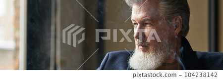 Portrait of thoughtful bearded mature businessman holding cigar and a glass of whisky while relaxing in loft interior 104238142