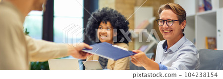 Cheerful man giving a folder with documents to his colleague and smiling while working together in the modern office 104238154