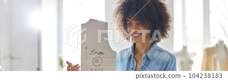 African-American lady holds sewing pattern standing at cutting table in workshop African-American lady holds sewing pattern standing at cutting table in workshop 104238183