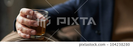 Successful middle aged business man holding glass of alcohol scotch whiskey in his hand while relaxing indoors. Focus on a drink 104238280