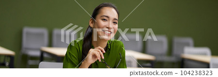 Business training. Young happy woman, female office worker sitting at desk in the office and smiling, listening to coach during corporate seminar Business training. Young happy woman, female office worker sitting at desk in the office and smiling, listening to coach during corporate seminar 104238323