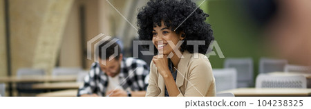 New skills. Happy mixed race businesswoman sitting at desk in the modern coworking space, listening to coach and smiling during corporate business training New skills. Happy mixed race businesswoman sitting at desk in the modern coworking space, listening to coach and smiling during corporate business training 104238325