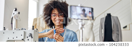 African-American lady holds blue threads shooting tutorial at sewing machine in workshop African-American lady holds blue threads shooting tutorial at sewing machine in workshop 104238333