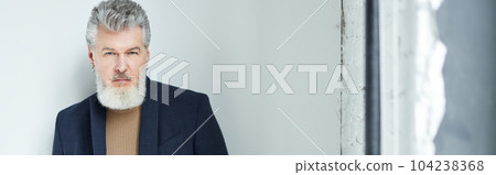 Stylish middle aged man in business casual wear looking at camera, adjusting his suit while posing against white background in loft interior 104238368