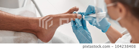 Woman master polishes toenail of male client with tool at procedure in beauty salon Woman master polishes toenail of male client with tool at procedure in beauty salon 104238408
