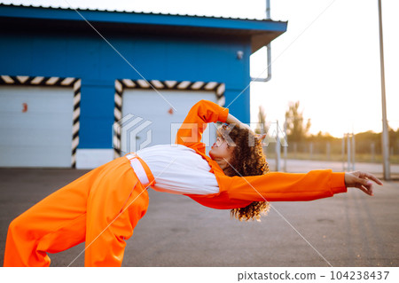 Young African American woman - dancer dancing in the street at sunset. Stylish woman with curly hair in an orange suit showing some moves 104238437