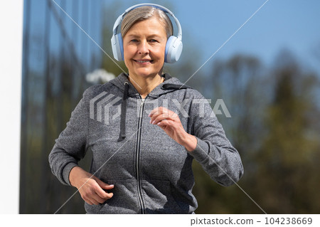 Woman in sportswear and headphones having morning run in the park Woman in sportswear and headphones having morning run in the park 104238669