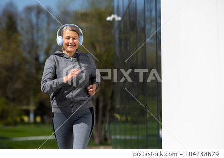 Woman in sportswear and headphones having morning run in the park Woman in sportswear and headphones having morning run in the park 104238679