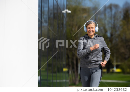 Woman in sportswear and headphones having morning run in the park 104238682