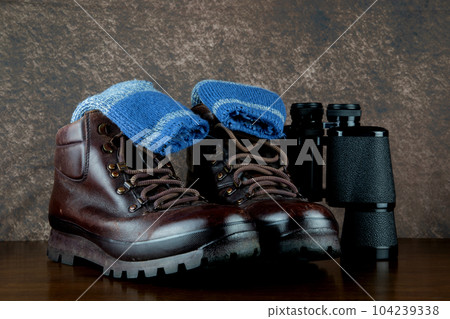 Hiking Boots and Socks with Binoculars on a Varnished Table Top 104239338