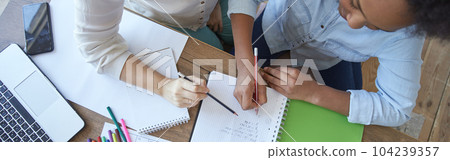 Top view of mixed race teen girl doing math task, school homework together with female teacher in the living room at home 104239357