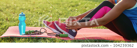 Adorable little girl in sportswear tying shoelaces outdoors Adorable little girl in sportswear tying shoelaces outdoors 104239362