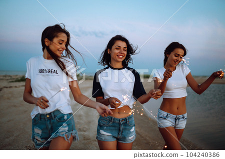 Three beautiful girls celebrating, holding sparklers on the beach at night. . Summer holidays, vacation. 104240386