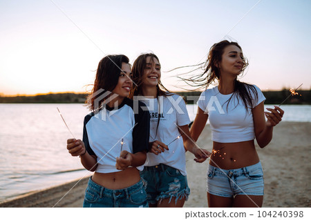 Three beautiful girls celebrating, holding sparklers on the beach at night. . Summer holidays, vacation. Three beautiful girls celebrating, holding sparklers on the beach at night. . Summer holidays, vacation. 104240398