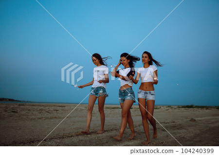 Three beautiful girls celebrating, holding sparklers on the beach at night. . Summer holidays, vacation. 104240399