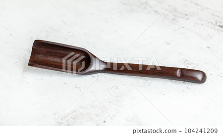 Narrow spice / tea spoon made of dark wood, on white working board. 104241209