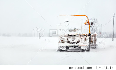 Orange plough truck on snow covered road, gray sky and trees in background, view from car driving behind Orange plough truck on snow covered road, gray sky and trees in background, view from car driving behind 104241218