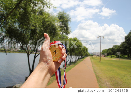 Blurred of woman hands raised and holding gold medals with Thai ribbon against blue sky background to show success in sport or business, Winners success award concept. 104241856