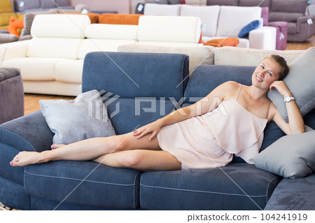 Cheerful woman with pillow on the sofa in furniture shop 104241919