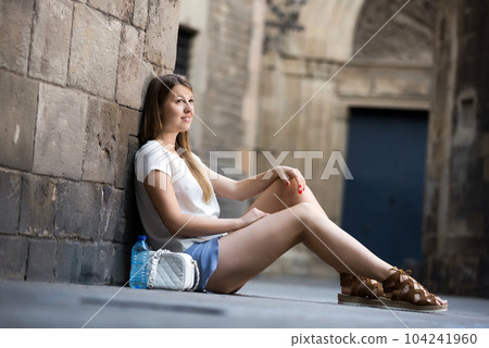 Young woman sitting near old stone wall 104241960