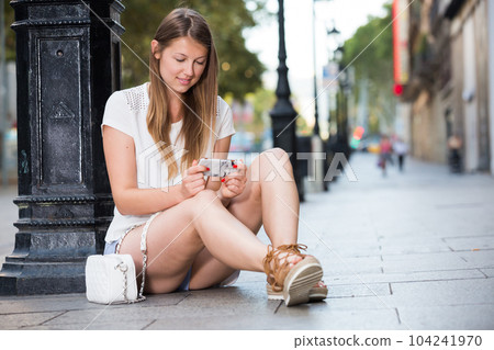 Girl using phone while relaxing near lamp post 104241970