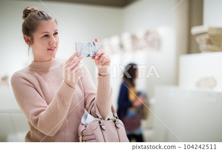 woman using smartphone and standing in art museum 104242511