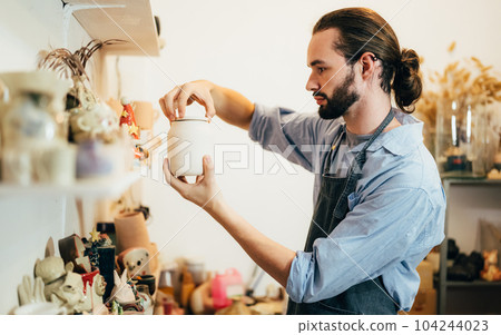 Craftsman potter making jug of clay on the potter's wheel circle in workshop 104244023