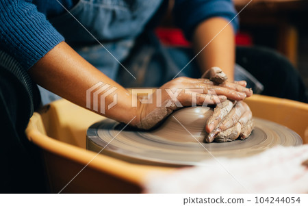 Craftsman potter making jug of clay on the potter's wheel circle in workshop 104244054