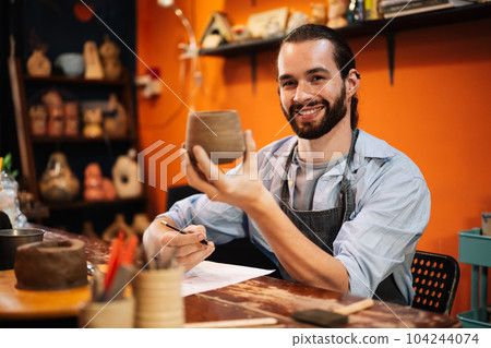 Craftsman potter making jug of clay on the potter's wheel circle in workshop 104244074