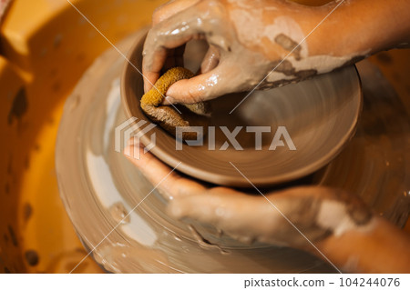 Close up on skillful hands sculpting pottery jar on potter wheel Close up on skillful hands sculpting pottery jar on potter wheel 104244076