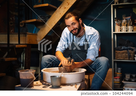 Craftsman potter making jug of clay on the potter's wheel circle in workshop Craftsman potter making jug of clay on the potter's wheel circle in workshop 104244094
