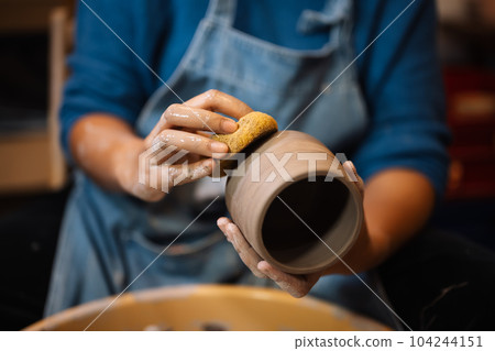 Close up on skillful hands sculpting pottery jar on potter wheel Close up on skillful hands sculpting pottery jar on potter wheel 104244151