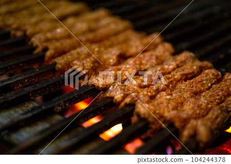 Making Spicy seekh kebabs are being grilled on burning charcoal in barbeque at a dinner party at night 104244378