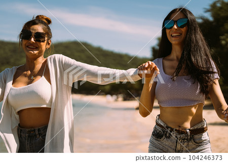 Portrait of two young female friends walking on sea shore happily Portrait of two young female friends walking on sea shore happily 104246373