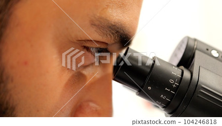 Eye of professional male scientist looking through microscope in laboratory 104246818