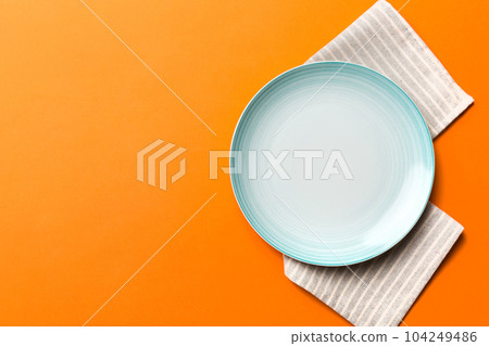 Top view on colored background empty round blue plate on tablecloth for food. Empty dish on napkin with space for your design Top view on colored background empty round blue plate on tablecloth for food. Empty dish on napkin with space for your design 104249486