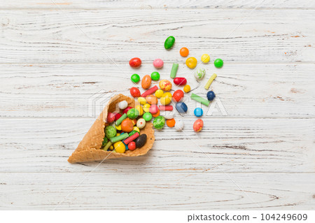 waffle cone full of assorted traditional candies falling out on colored background with copy space. Happy Holidays sale concept waffle cone full of assorted traditional candies falling out on colored background with copy space. Happy Holidays sale concept 104249609