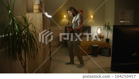 Man plays guitar in bedroom. 104250457