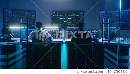 Diverse IT technical specialists work on computers in monitoring office 104250584