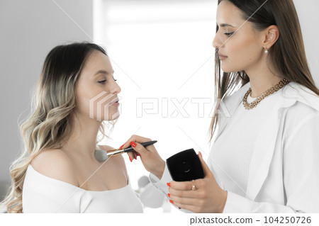 The makeup artist uses his creativity and skills to create a unique makeup that emphasizes the best features young woman's face, neck and chest and emphasizes her style. White color in beauty salon The makeup artist uses his creativity and skills to create a unique makeup that emphasizes the best features young woman's face, neck and chest and emphasizes her style. White color in beauty salon 104250726