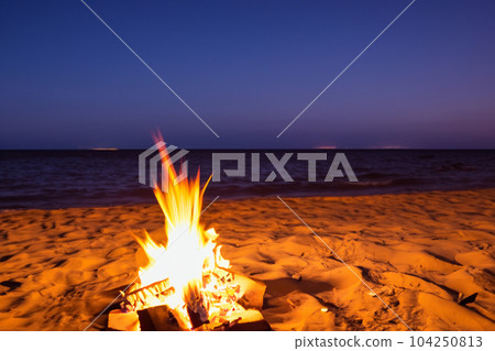 Bonfire. Small campfire with gentle flames beside a lake during a glowing sunset. San Juan night on the beach. People jumping over the bonfires. Bonfire at night. Bonfire. Small campfire with gentle flames beside a lake during a glowing sunset. San Juan night on the beach. People jumping over the bonfires. Bonfire at night. 104250813