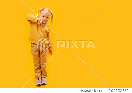 Full length portrait of girl shows finger down. Child of 4-5 years old in yellow suit on bright yellow background . Copy space, mock up Full length portrait of girl shows finger down. Child of 4-5 years old in yellow suit on bright yellow background . Copy space, mock up 104252783